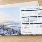 Novoročenka 588 – Zimní klid s kalendářem – PF 2027, zasněžené hory, jezero a les v ranním světle, DL na šířku s kalendářem 2027, ilustrační zátiší