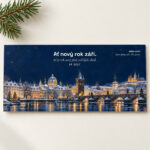 Novoročenka 603 – Zimní město – PF 2027, osvětlená zasněžená Praha a Karlův most za zimního večera, DL na šířku, ilustrační zátiší